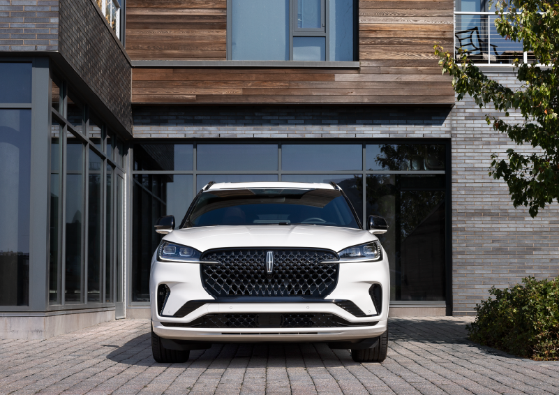 A white 2025 Lincoln Aviator® SUV is shown parked outside a modern building with gray brick and wood accents. | Palmetto Lincoln in Charleston SC