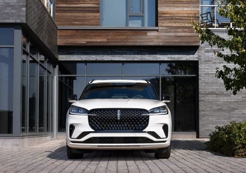 A white 2025 Lincoln Aviator® SUV is shown parked outside a modern building with gray brick and wood accents. | Palmetto Lincoln in Charleston SC