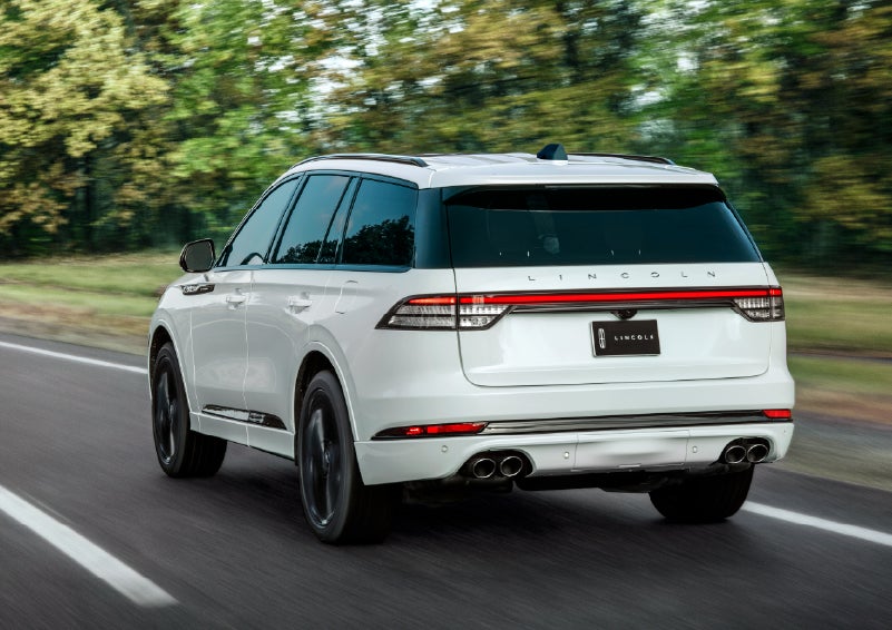A white 2026 Lincoln Aviator® SUV is being driven away down a road lined with colorful trees. | Palmetto Lincoln in Charleston SC