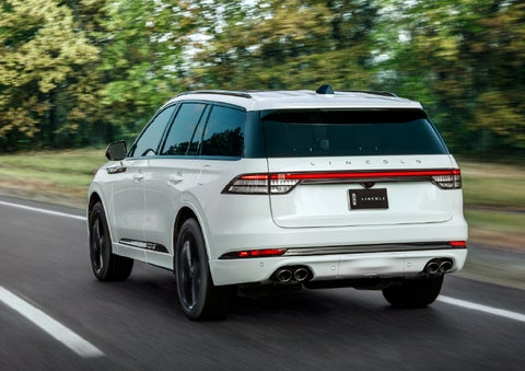 A white 2026 Lincoln Aviator® SUV is being driven away down a road lined with colorful trees. | Palmetto Lincoln in Charleston SC