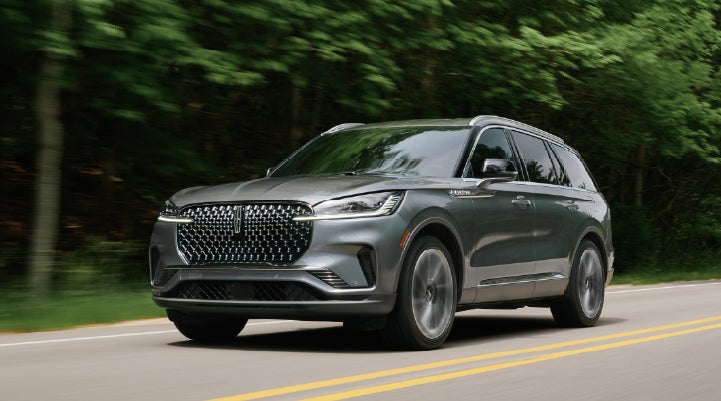 A 2027 Lincoln Aviator® SUV is being driven down a road lined with trees. | Palmetto Lincoln in Charleston SC